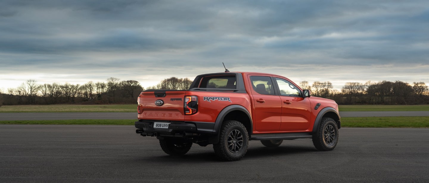 Der Ford Ranger Raptor in Rot. Dreiviertelansicht, stehend auf einem Parkplatz bei Sonnenuntergang.