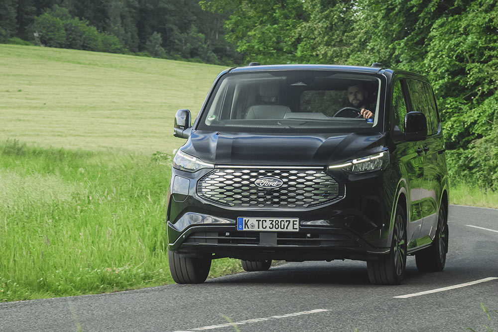 Ford E-Tourneo Custom in Schwarz. Frontansicht, fährt auf einer Landstraße.
