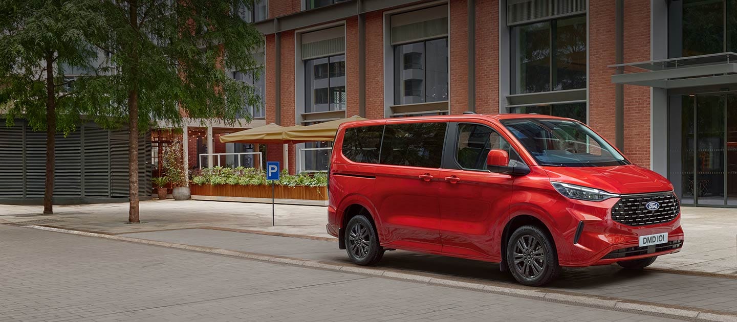 Ford Tourneo Custom in Rot. Dreiviertelansicht, parkend vor einem Gebäude.