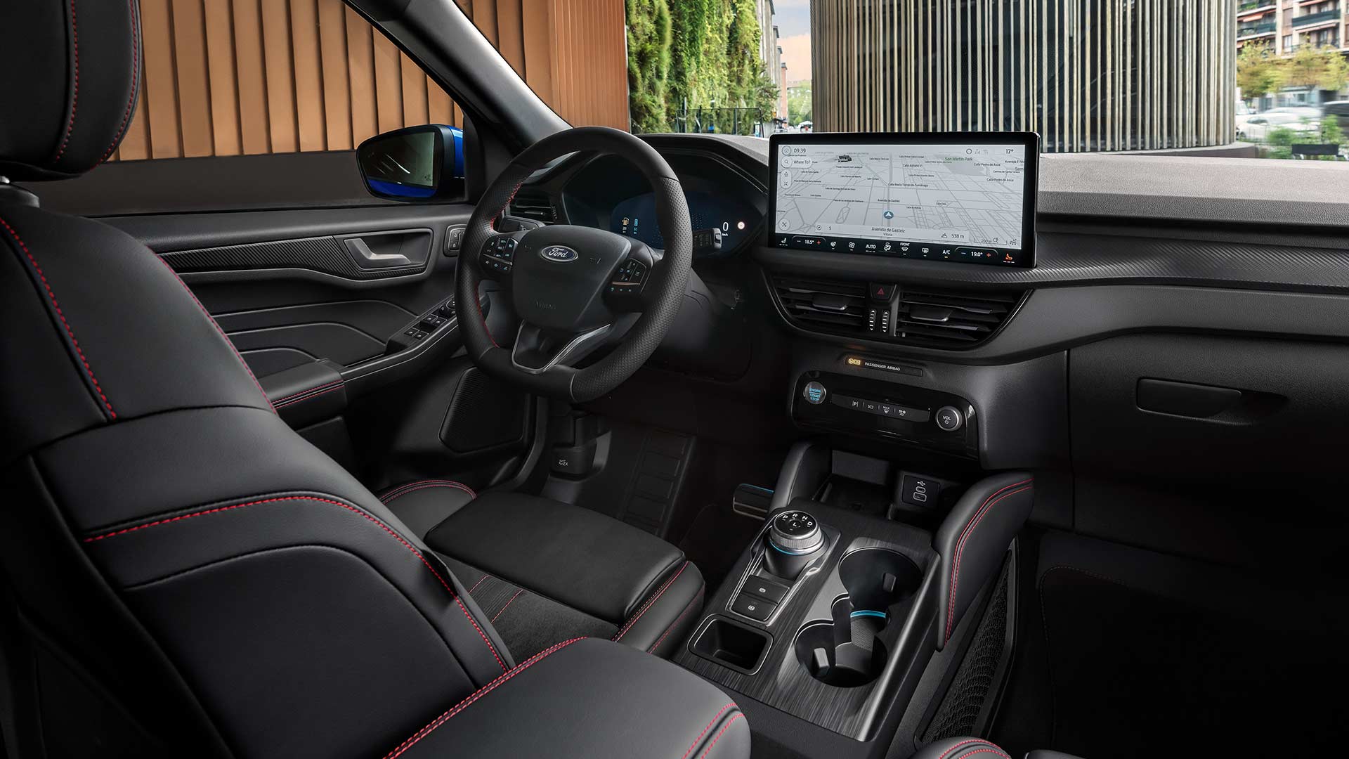 Ford Kuga Innenraum. Ansicht des Lenkrads mit Ford Logo, dem großen SYNC® 4-Touchscreen und den schwarzen Sitzen mit roten Nähten.