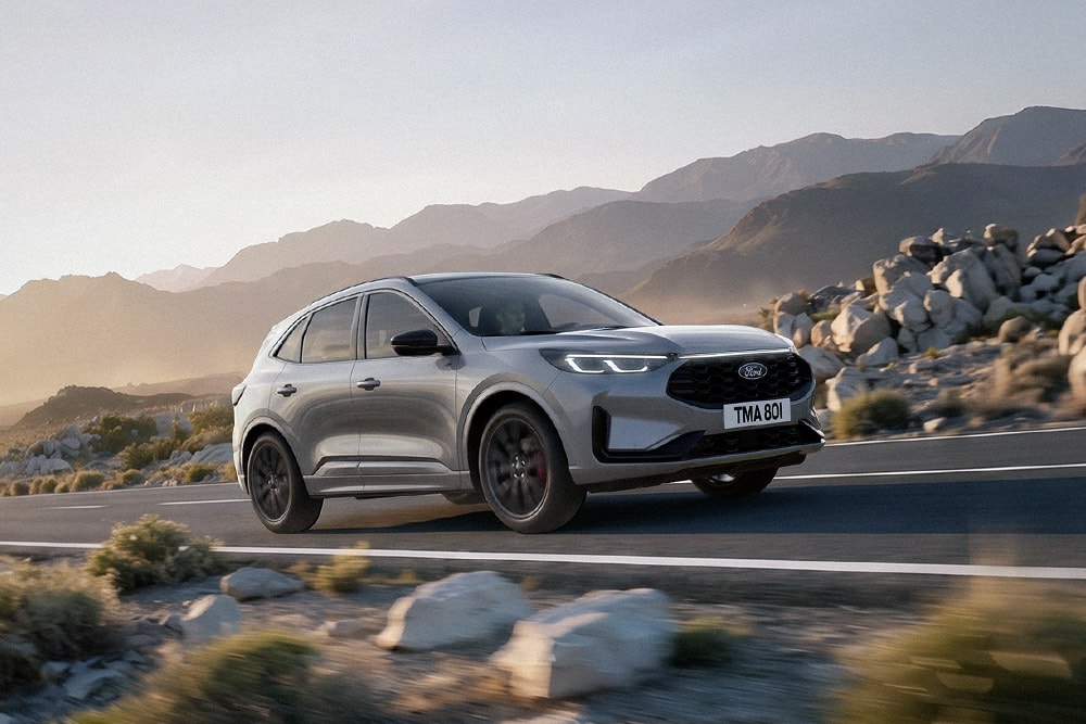 Ford Kuga in Silber. Frontansicht, bei der Fahrt durch eine felsige Berglandschaft.