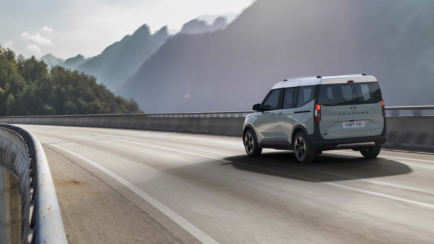 Ford E-Tourneo Courier in Grau. Heckansicht, fahrend auf einer Brücke.