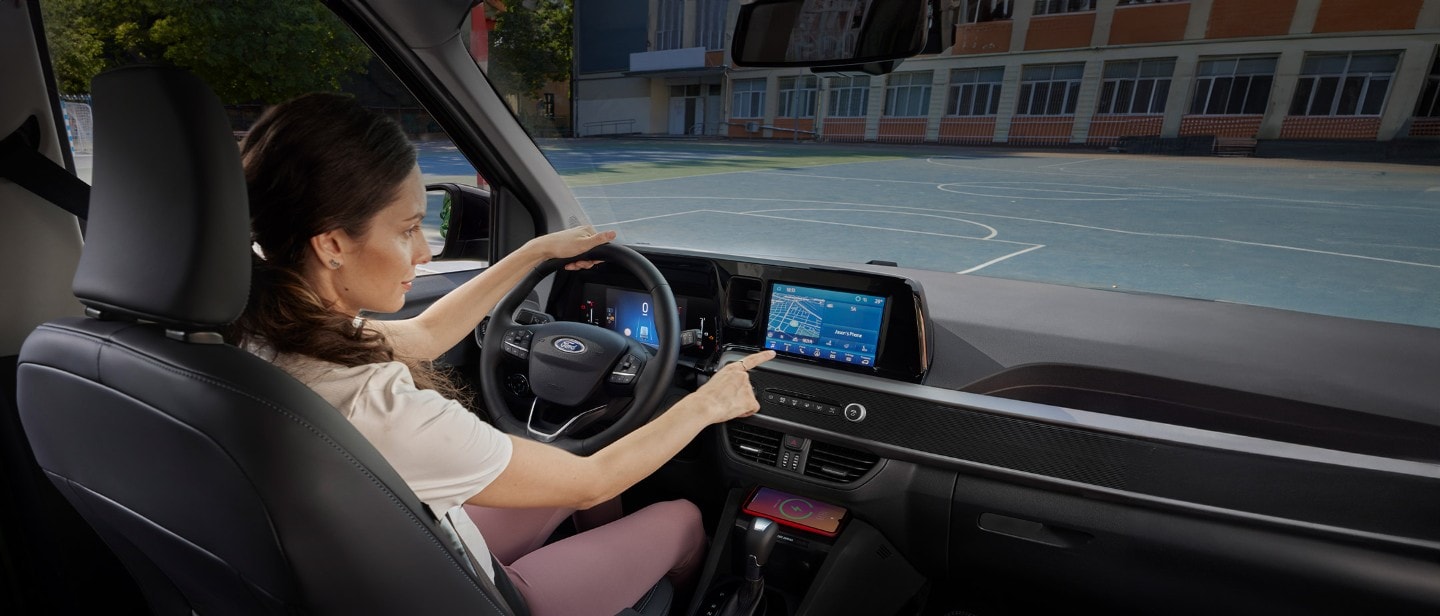 Ford Tourneo Courier Innenraum. Ansicht auf Vordersitz und Armaturenbrett mit Ford SYNC 4-Touchscreen. Frau sitzt im Fahrersitz.
