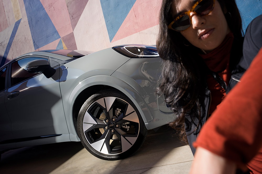 Ford Puma in Grau. Dreiviertelansicht, stehend vor einer bunten Wand. Person posiert im Vordergrund.