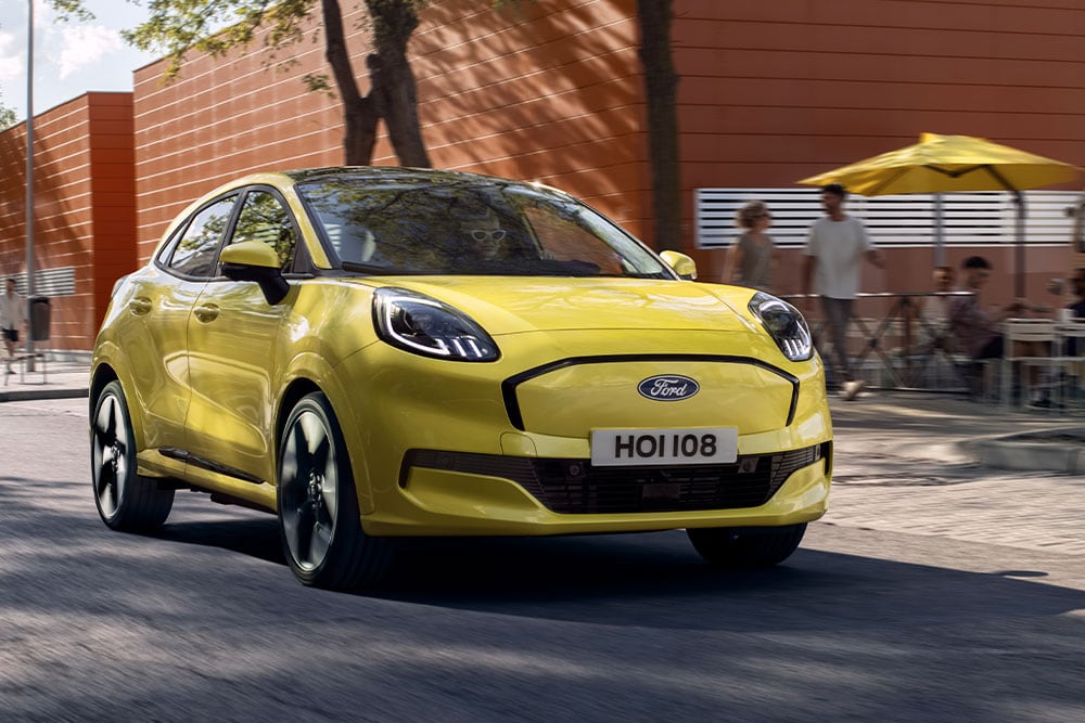 Ford Puma Gen-E in Gelb. Dreiviertelansicht, fahrend durch eine Straße.