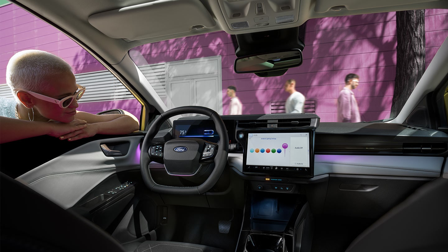 Ford Puma Gen-E Innenraum. Ansicht auf Instrumententafel, Lenkrad und SYNC 4-Touchscreen. Person lehnt sich in das Fenster.