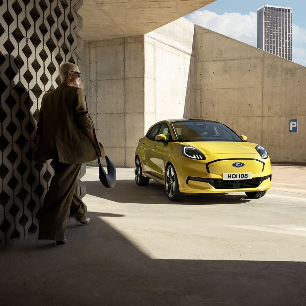 Ford Puma Gen-E in Gelb. Dreviertelansicht, Person nähert sich dem Fahrzeug.