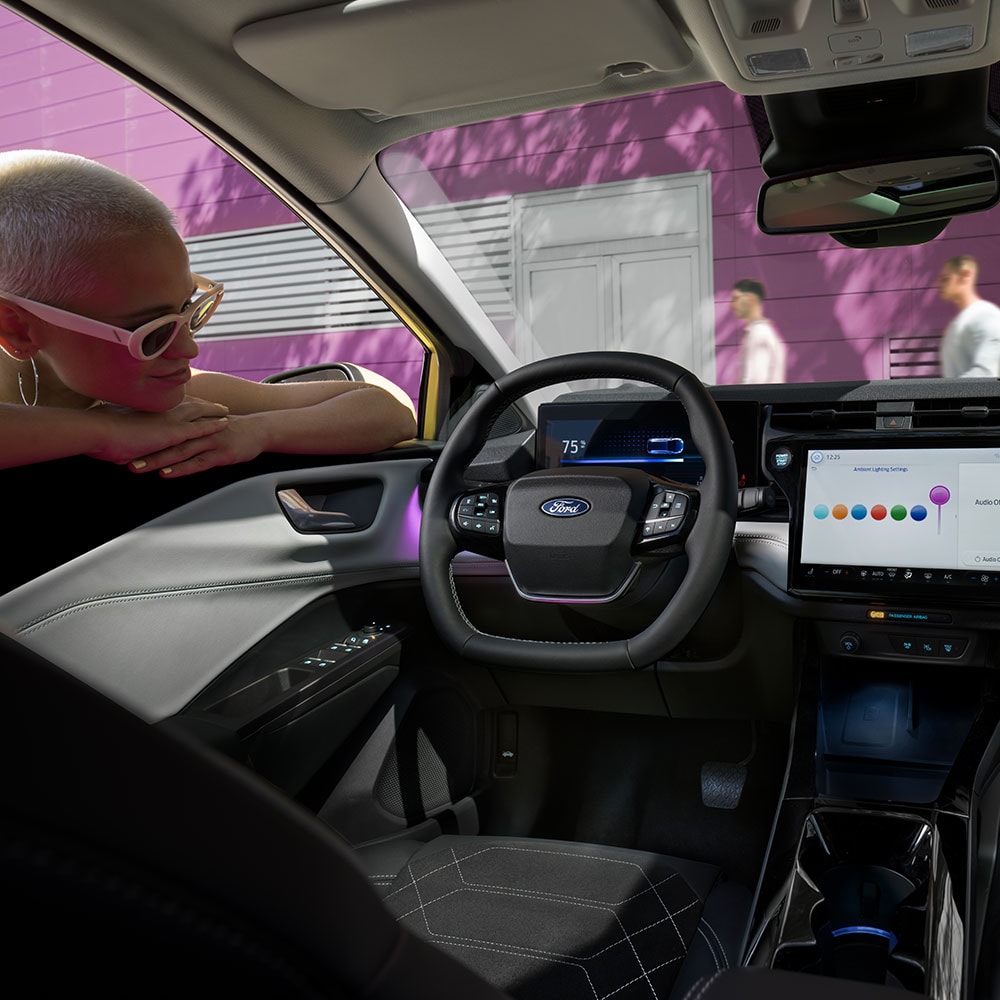 Ford Puma Gen-E Innenraum. Ansicht auf Instrumententafel, Lenkrad und SYNC 4-Touchscreen. Person lehnt sich in das Fenster.