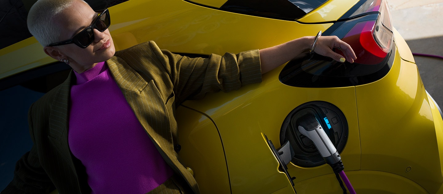 Ford Puma Gen-E in Gelb. Detailansicht des Ladeanschlusses mit Kabel. Person lehnt an dem Auto. 