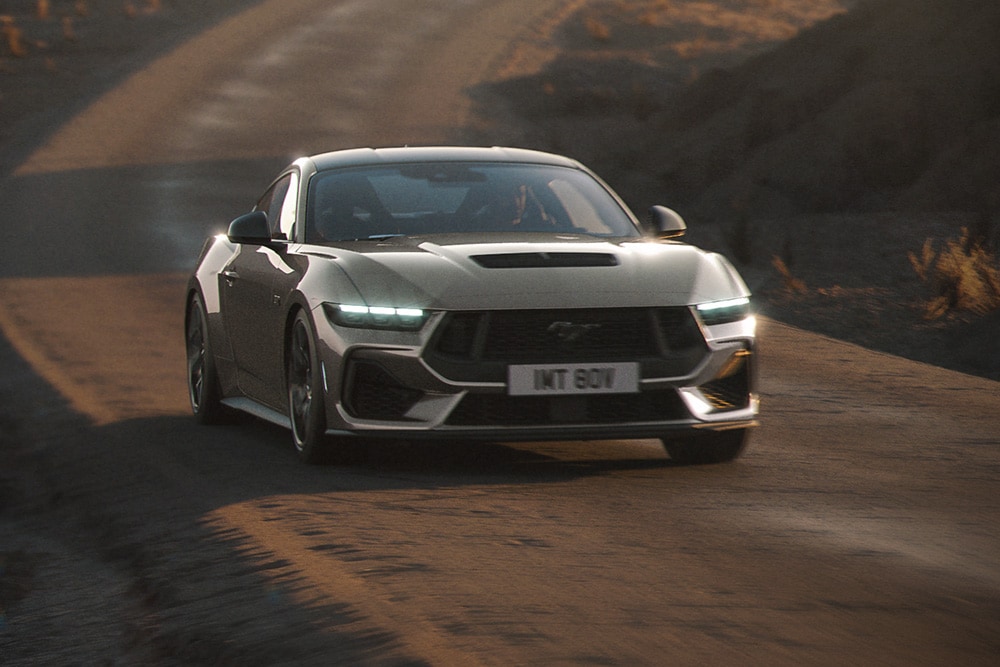 Ford Mustang GT in Grau. Frontansicht, fahrend auf einer unebenen Straße.