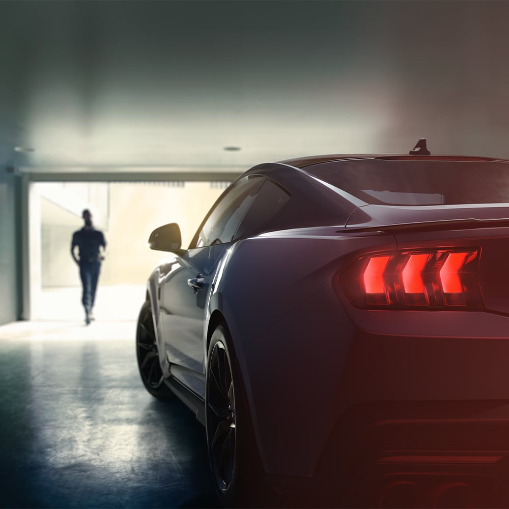 Ford Mustang in Blau. Heckansicht, parkend in einer Garage. Mann im Hintergrund.