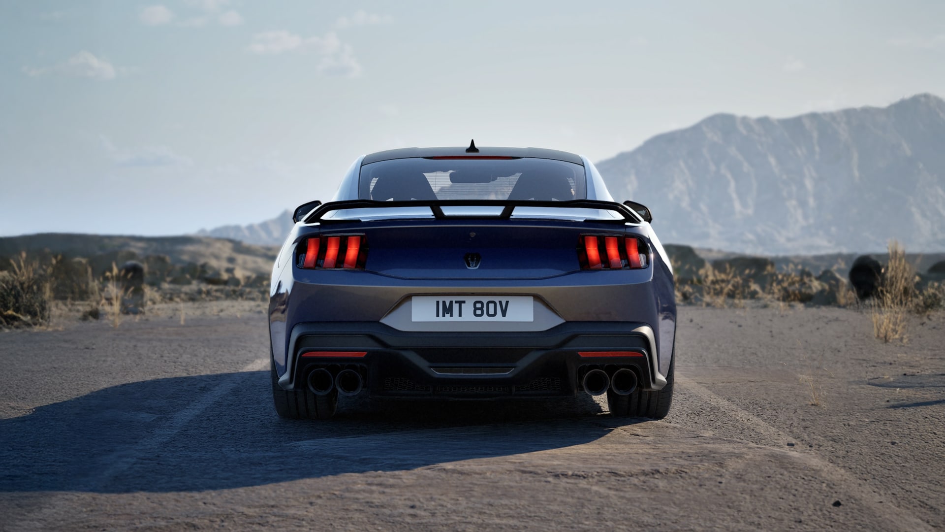 Ford Mustang in Blue Ember Metallic. Heckansicht, stehend auf einer Straße. Hügel im Hintergrund. 