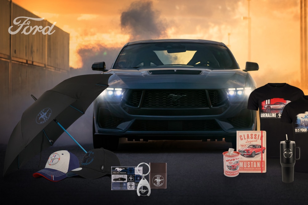 Ford Mustang Kollektion. Im Hintergrund ein grauer Ford Mustang und davor Mustang Werbeartikel wie ein Regenschirm, Kappen, Tassen und T-Shirts.