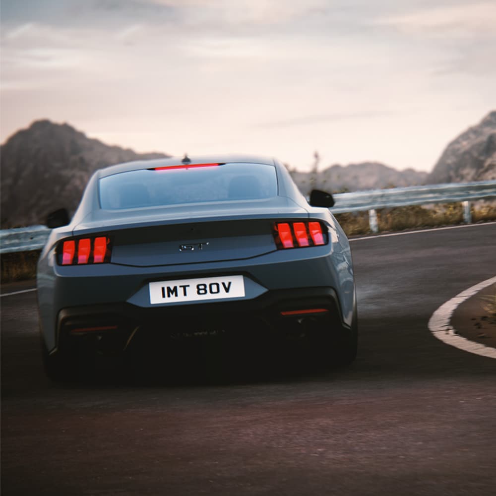Ford Mustang in Blau. Dreiviertelansicht, fahrend auf einer unbefestigten Straße bei Sonnenuntergang.