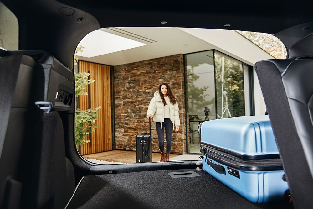 Ford Explorer – Detailansicht des Kofferraums mit einem blauen Koffer. Person geht zum Fahrzeug.