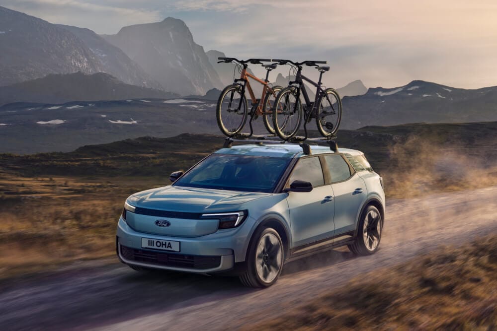 Ford Explorer in Blau. Dreiviertelansicht, fährt durch eine Berglandschaft mit Fahrradträger auf dem Dach.