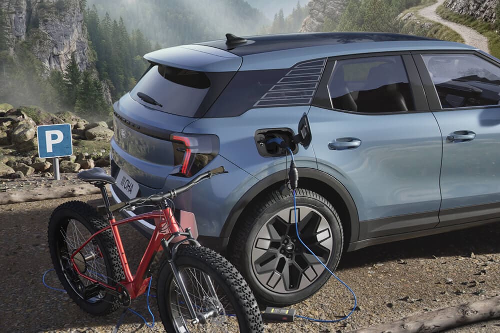 Ein E-Bike wird an einem blauen Ford Explorer aufgeladen, im Hintergrund eine Berglandschaft.