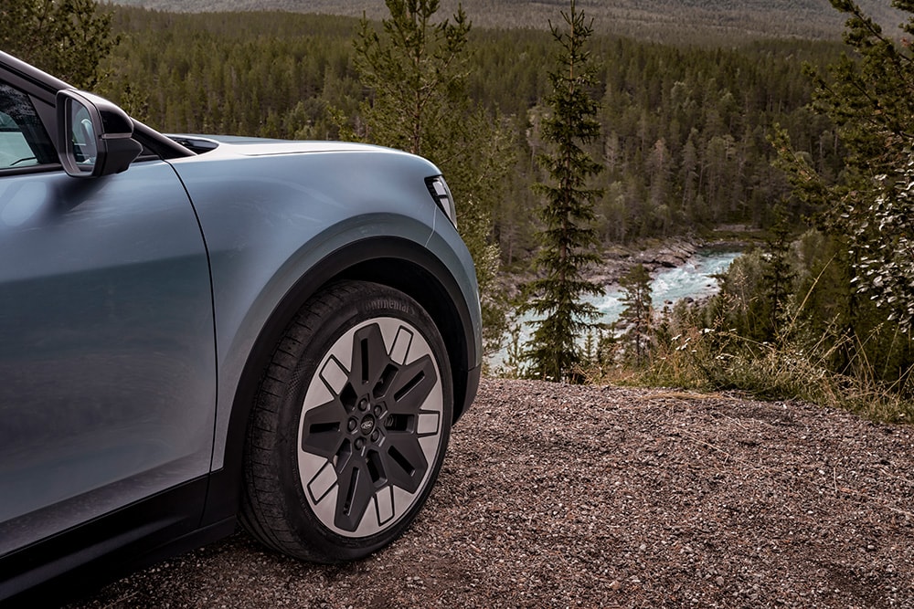 Der vollelektrische Ford Explorer in Blau. Ansicht auf Rückspiegel und Vorderrad. Wald im Hintergrund.