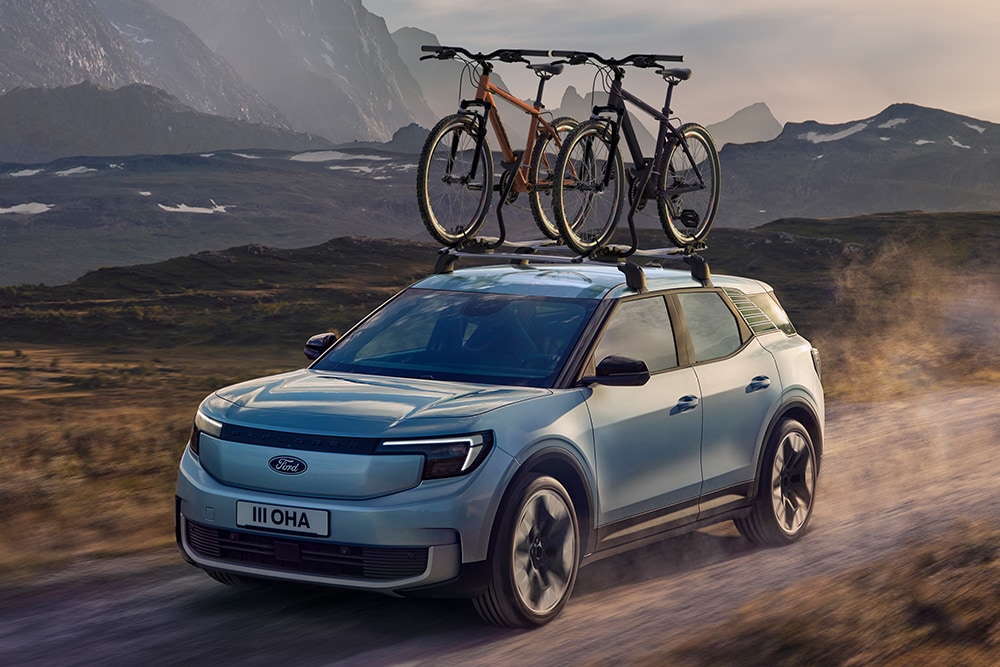 Ford Explorer in Blau. Dreiviertelansicht, fahrend auf einer Straße mit zwei am Dachträger befestigten Fahrrädern.