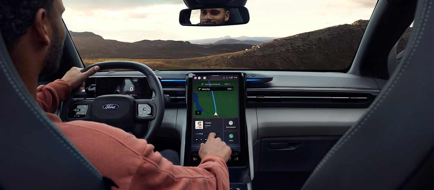 Der vollelektrische Ford Explorer Innenraum. Ansicht auf Lenkrad. Mann bedient den Ford SYNC Move-Touchscreen.