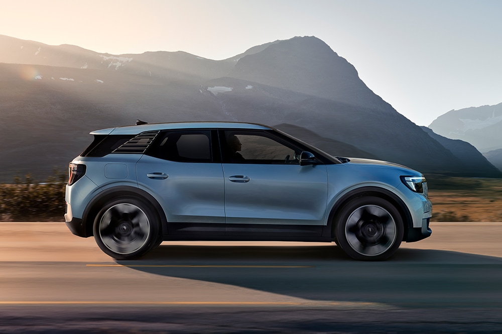 Ford Explorer in Blau. Seitenansicht, fahrend auf einer Straße bei Sonnenuntergang. Berge im Hintergrund.