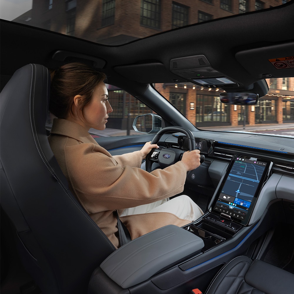 Der vollelektrische Ford Explorer Innenraum. Ansicht auf Lenkrad, Ford SYNC Move-Touchscreen und Panoramadach. Frau sitzt im Fahrersitz.
