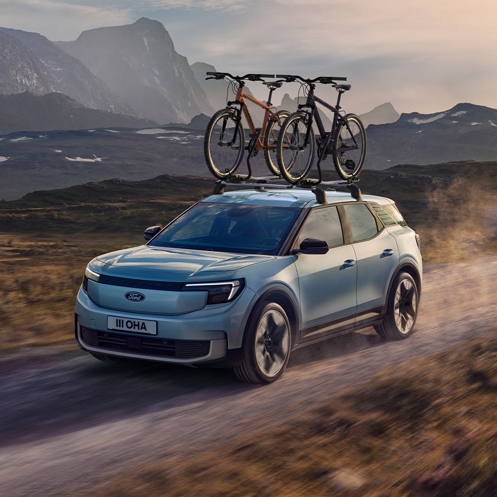 Ford Explorer in Blau. Dreiviertelansicht, fahrend auf einer Straße mit zwei am Dachträger befestigten Fahrrädern.