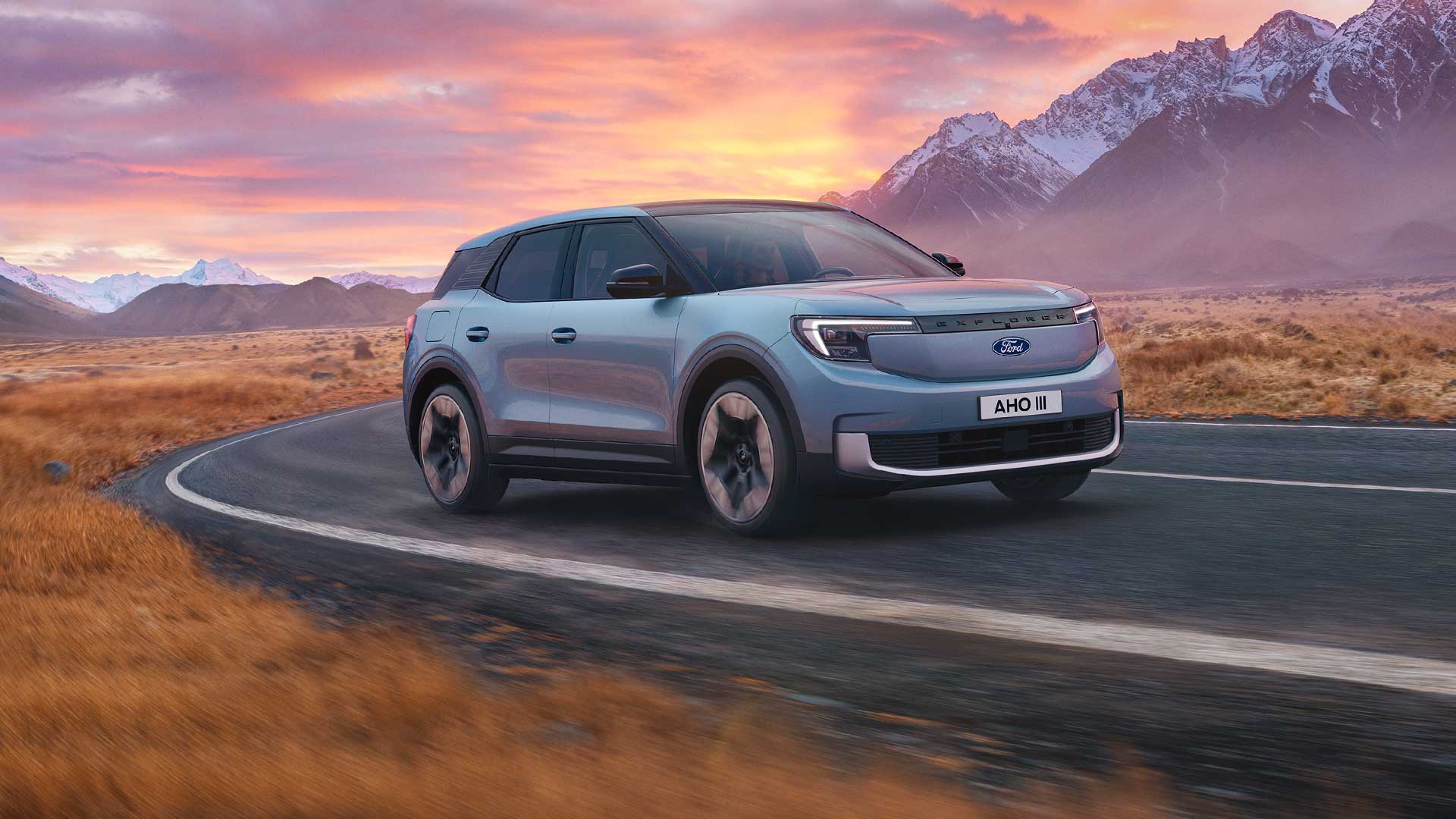 Ford Explorer in Blau. Dreiviertelansicht, fährt bei Sonnenuntergang eine Straße entlang. Berge im Hintergrund.