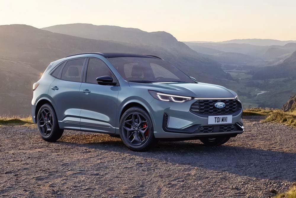 Ein blauer Ford Kuga. Dreiviertelansicht, parkt bei Sonnenuntergang auf einer Schotterstraße.