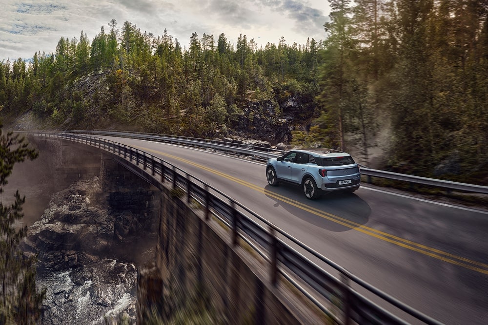 Ford Explorer in Blau. Der Ford Familien SUV fährt eine Straße mit Waldlandschaft entlang.