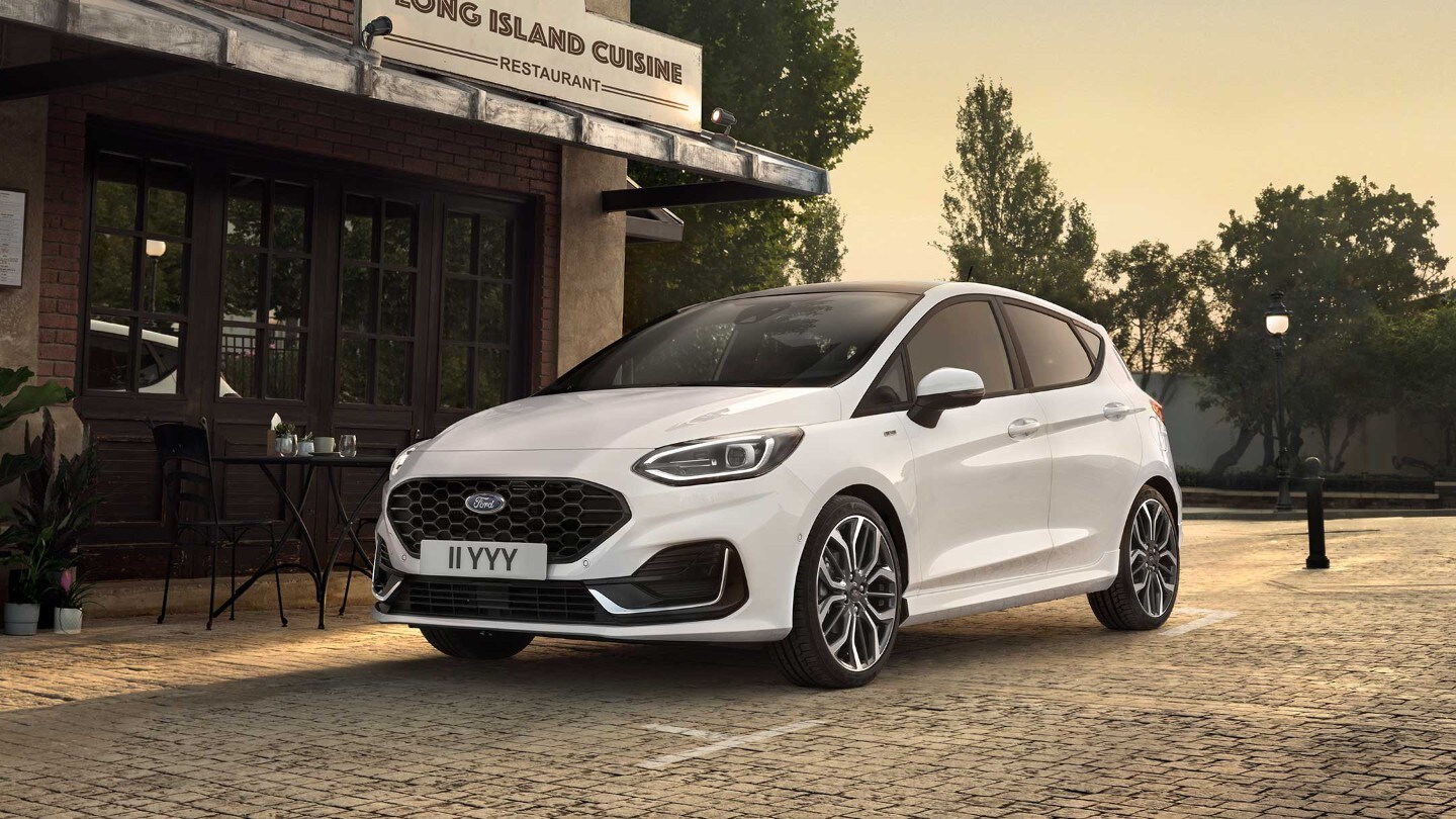 Ford Fiesta in Weiß. Dreiviertelansicht, parkt neben einem Restaurant