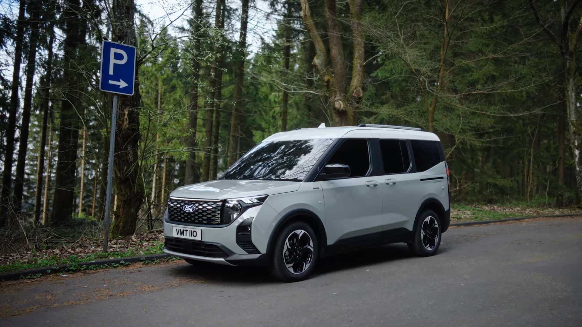 Ford E-Tourneo Courier in Silber. Dreiviertelansicht, stehend vor einem Wald.