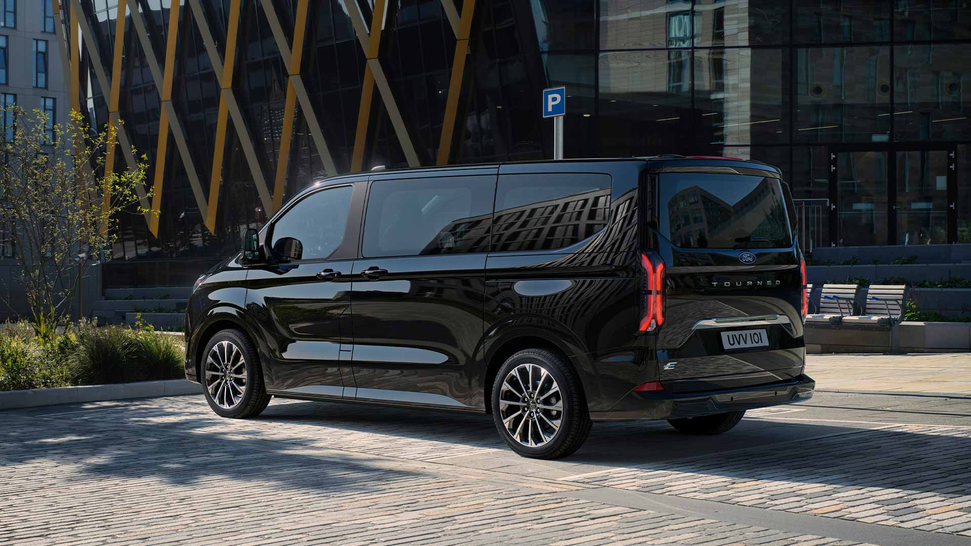 Ford Tourneo Custom in Schwarz. Dreiviertelansicht, parkend vor einem Gebäude.