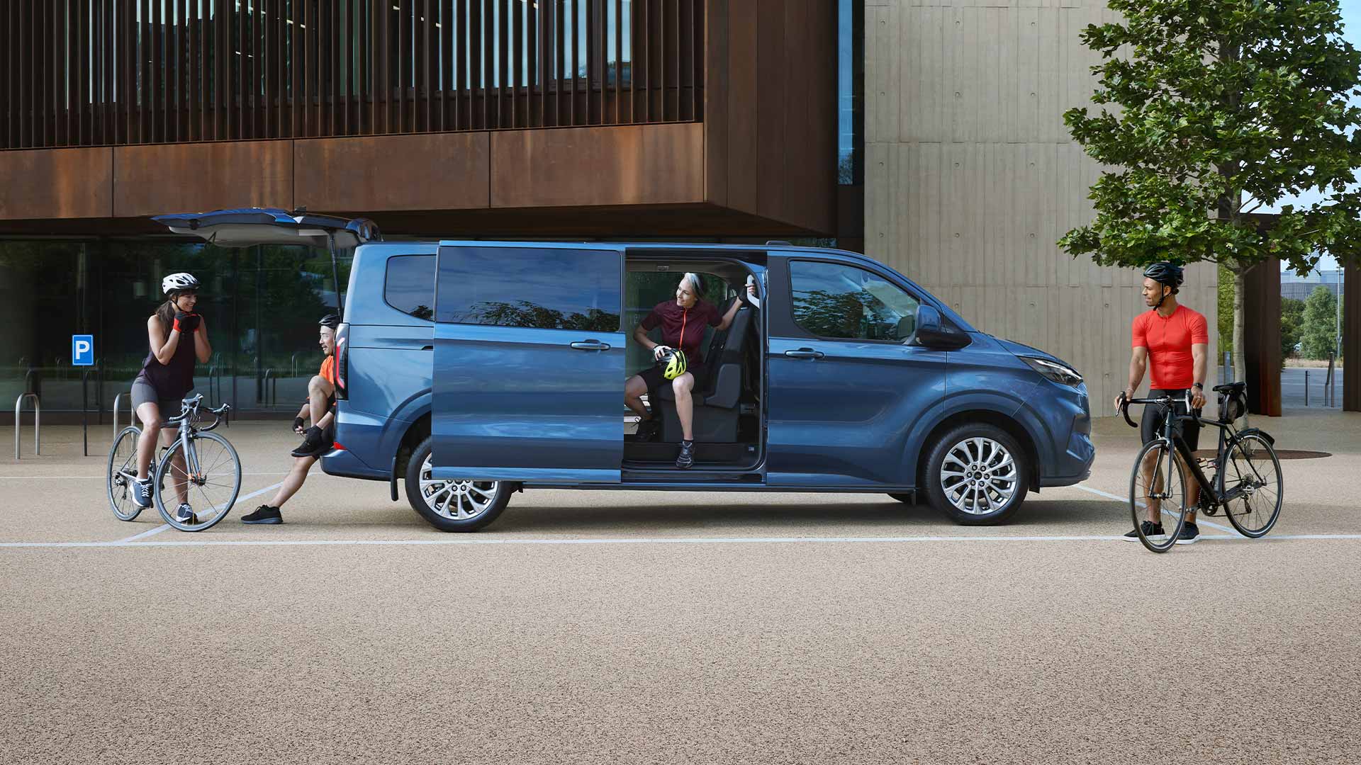Ford Tourneo Custom in Blau. Seitenansicht, stehend vor einem Haus mit geöffneter Seitentür.