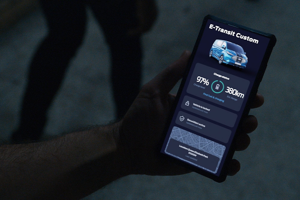 Eine Hand hält ein Smartphone mit geöffneter FordPass App, die den Ladestand eines Fahrzeugs anzeigt. 