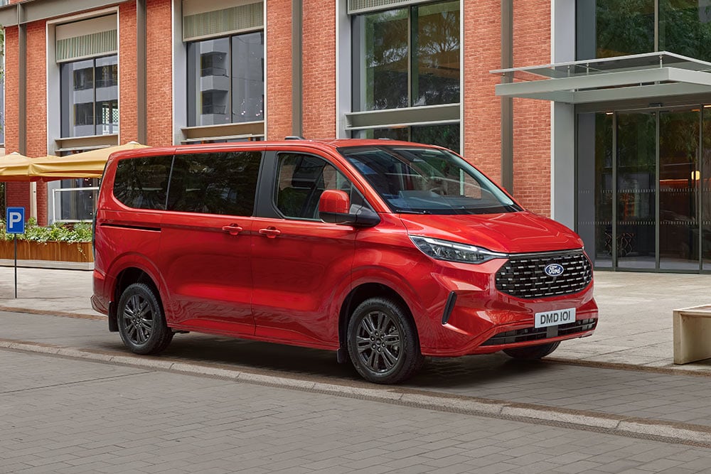 Ford Tourneo Custom in Rot. Dreiviertelansicht, parkend vor einem Gebäude.