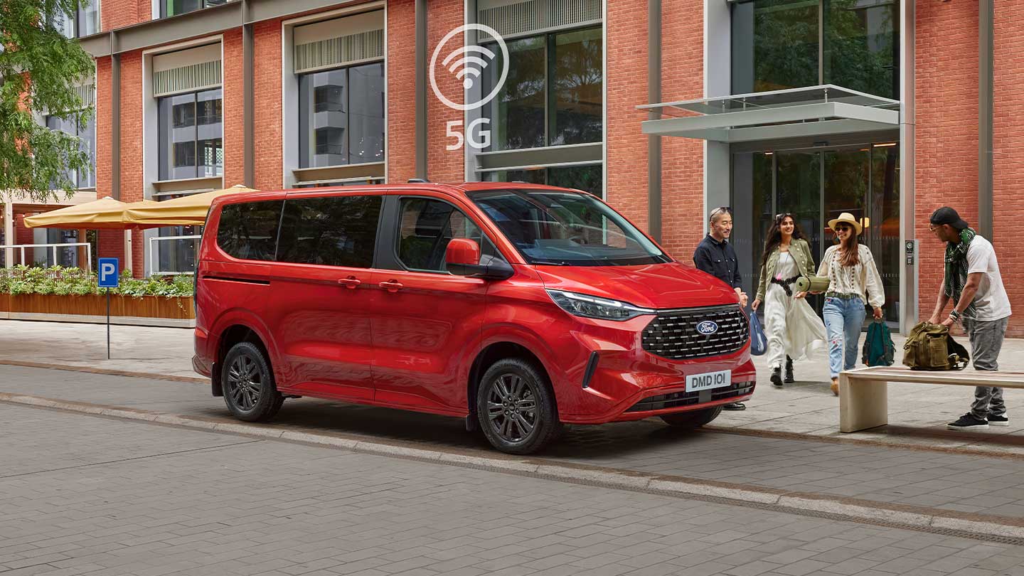Ford Tourneo Custom in Rot. Dreiviertelansicht, parkend vor einem Gebäude.