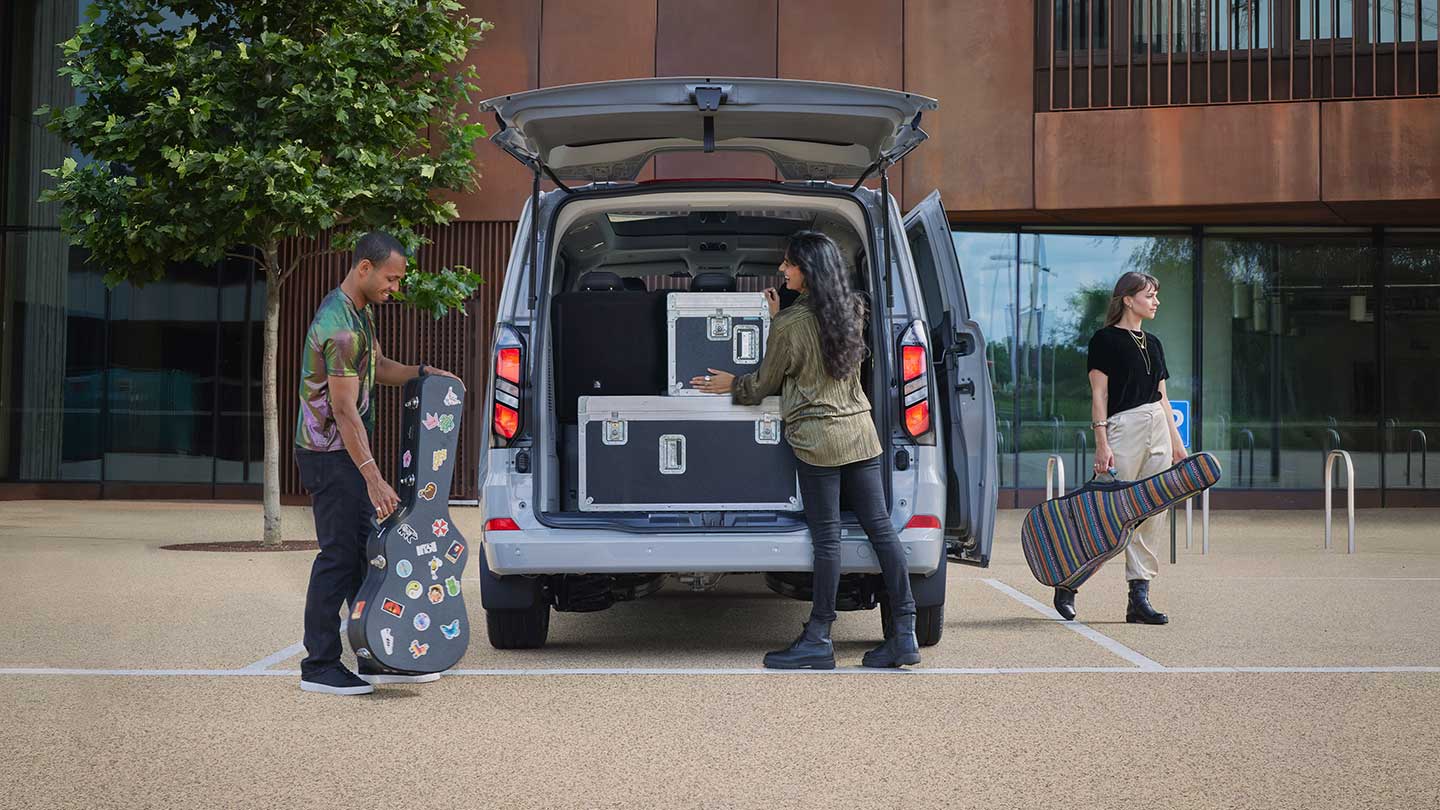 Ford Tourneo Custom in Silber. Ansicht auf geöffneten Kofferraum. Frau beladet das Fahrzeug.