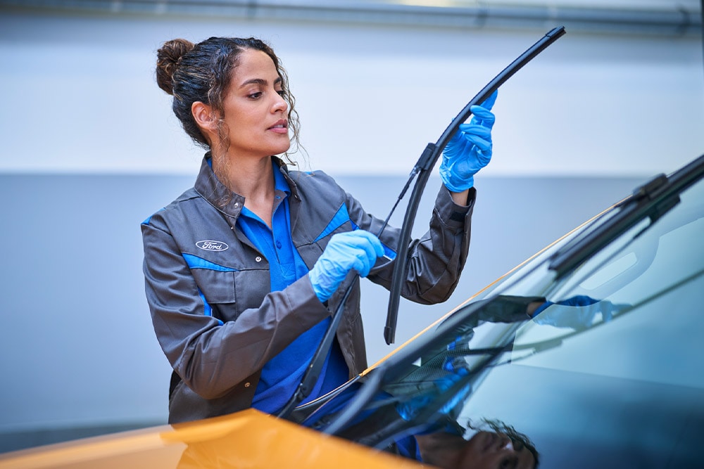 Ein Ford Techniker mit blauen Handschuhen stellt einen Scheibenwischer an einem Fahrzeug ein. 