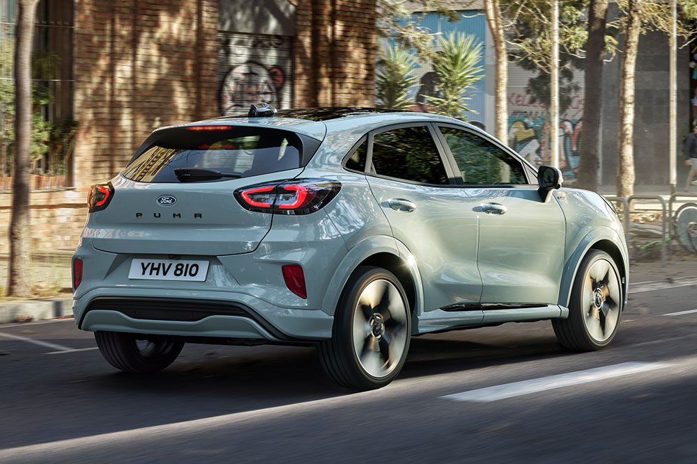 Heckansicht eines grauen Ford Puma, der auf einer Stadtstraße mit Menschen und Gebäuden fährt.