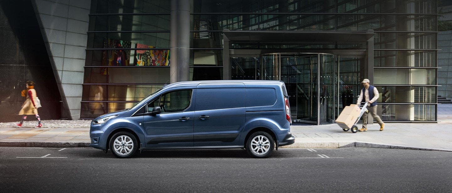 Ford Transit Connect in Blau. Seitenansicht, parkt vor einem Glasgebäude