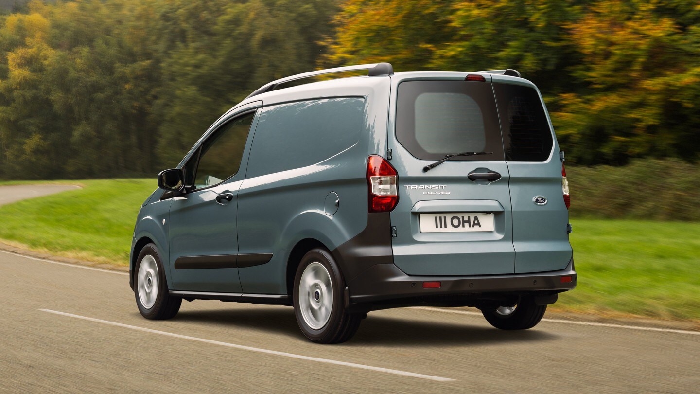 Ford Transit Courier in Blau. Dreiviertelansicht von hinten, fahrend auf einer Landstraße