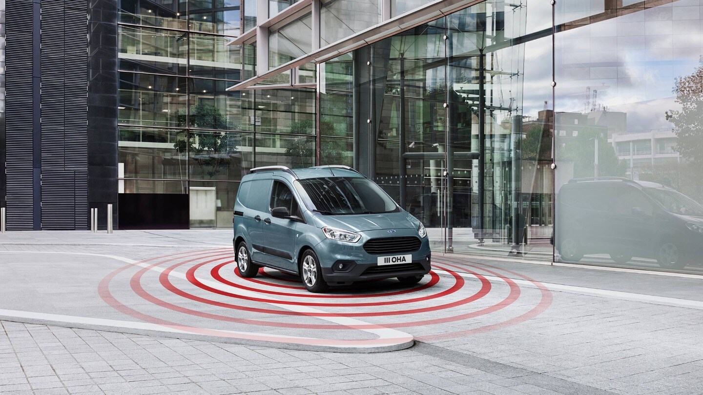 Ford Transit Courier in Blau. Dreiviertelansicht von vorne, fahrend vor einem modernen Gebäude. Illustration ESP