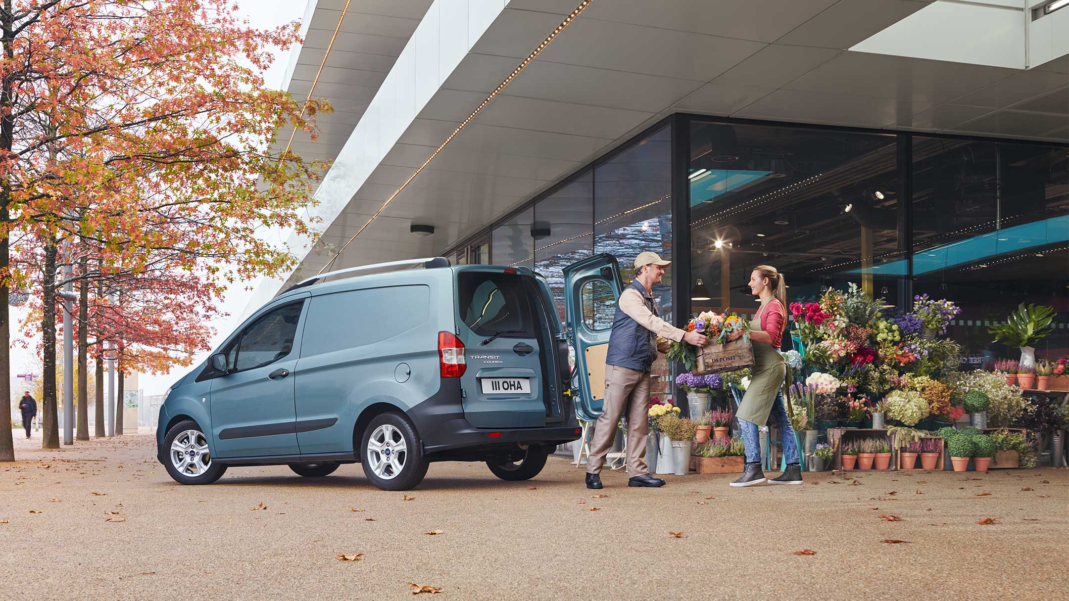 Ford Transit Courier in Blau. Dreiviertelansicht von hinten, parkend vor einem Blumengeschäft 
