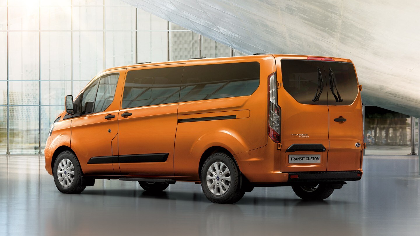 Ford Transit Custom Kombi in Orange. Dreiviertelansicht von hinten, parkend in einer Ausstellungshalle 