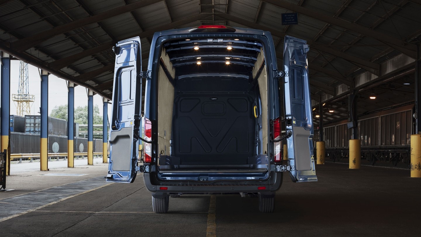 Ford Transit Kastenwagen in Blau. Heckansicht, parkend unter einem Vordach mit weit geöffneten Hecktüren