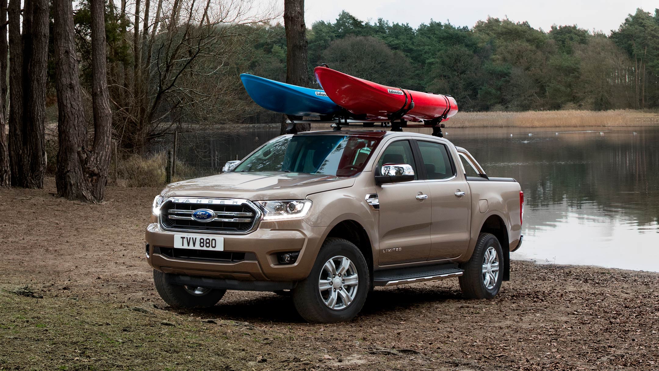 Ford Ranger in Silber. Dreiviertelansicht, parkend am Ufer eines Sees mit Kanus beladen