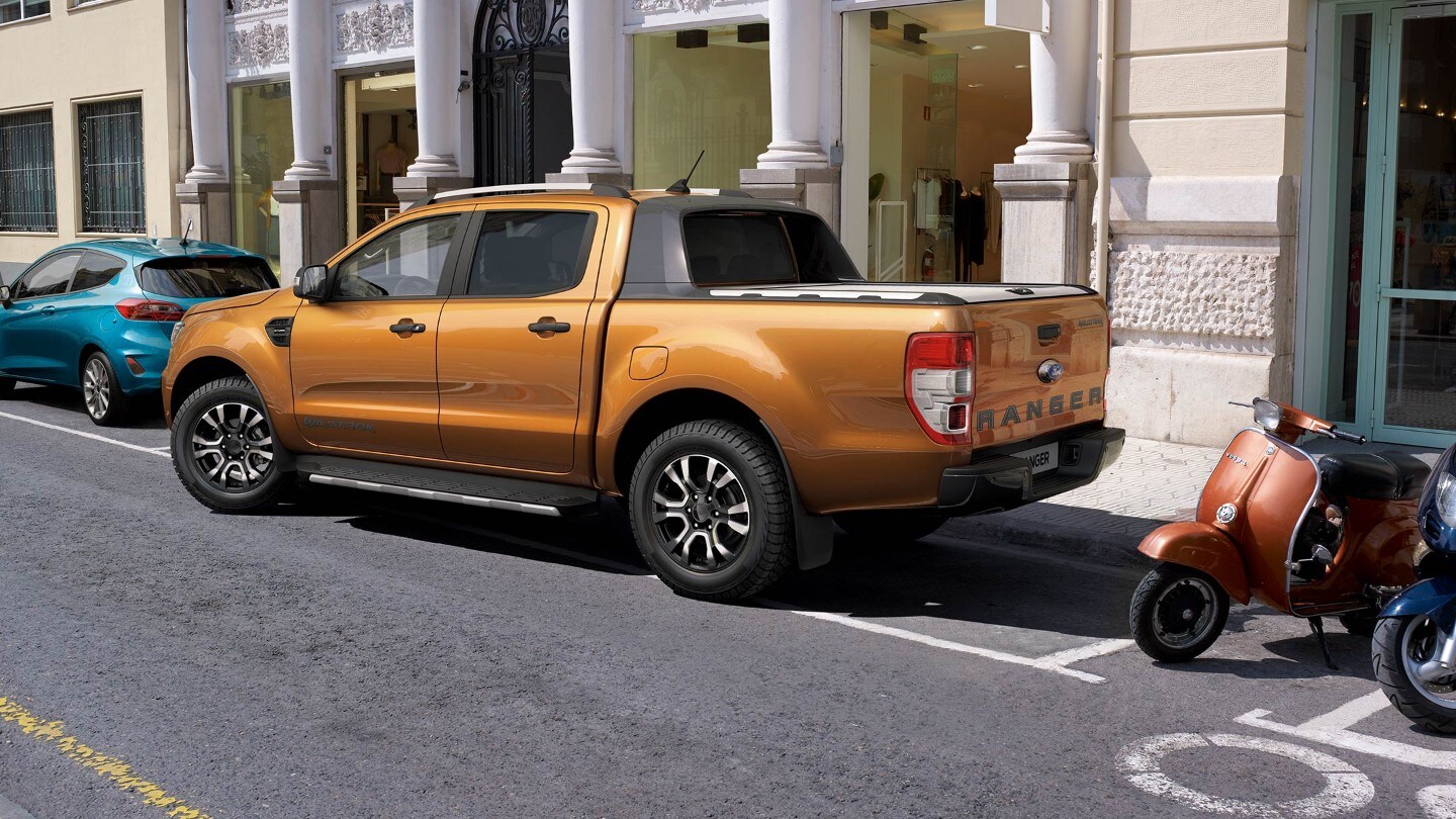 Ford Ranger in Orange. Dreiviertelansicht von hinten, seitlich einparkend in einen Parkplatz