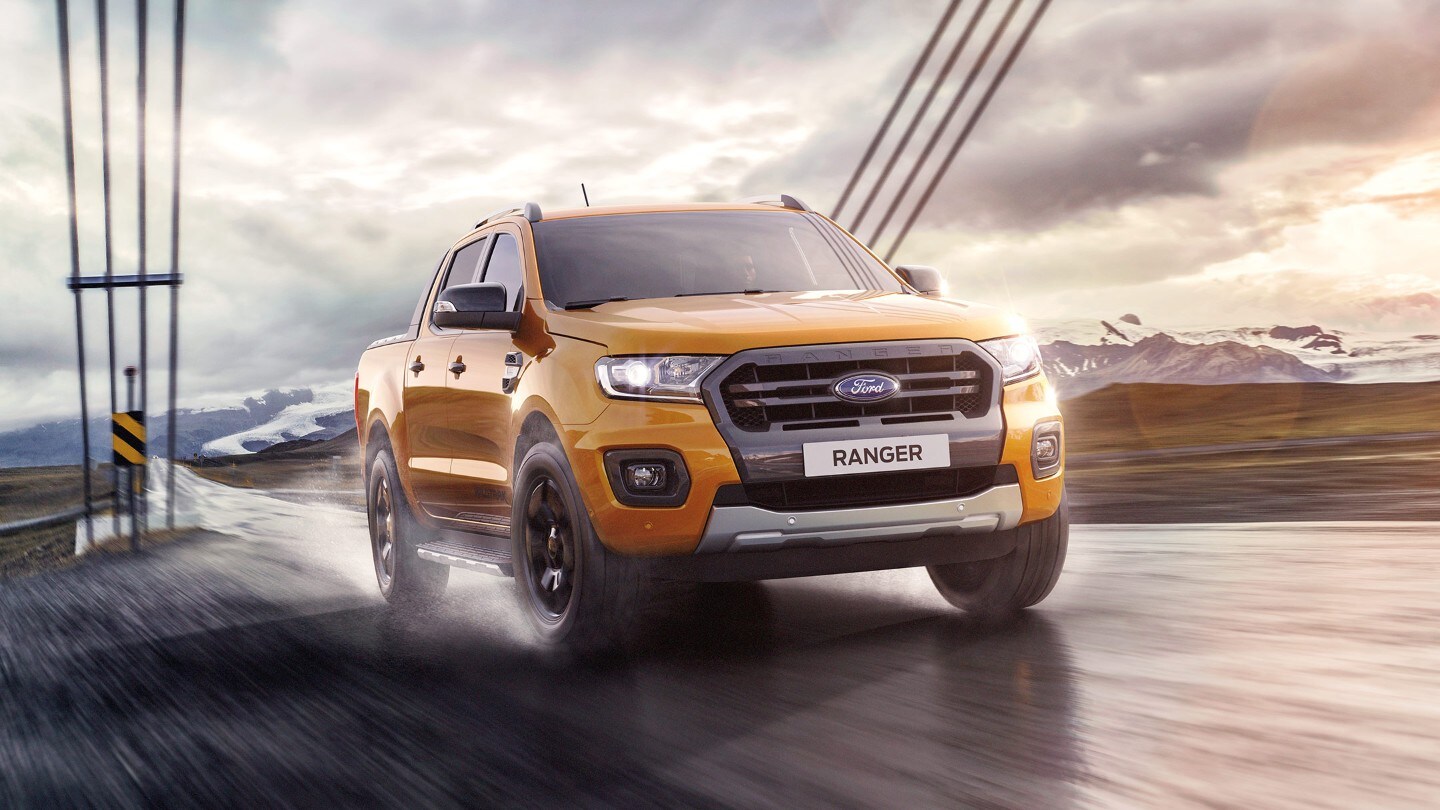 Ford Ranger in Orange. Frontansicht, auf nasser Straße fahrend