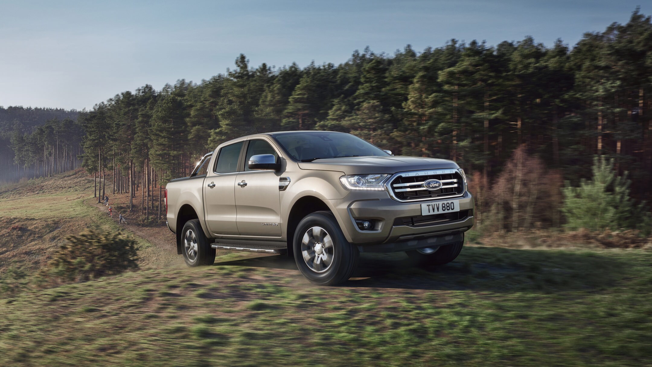 Ford Ranger in Silber. Dreiviertelansicht, auf einer Wiese in der Nähe eines Waldes